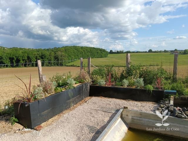 Jardinières en bois, massifs plantés et allée gravillonnée avec vue sur la campagne